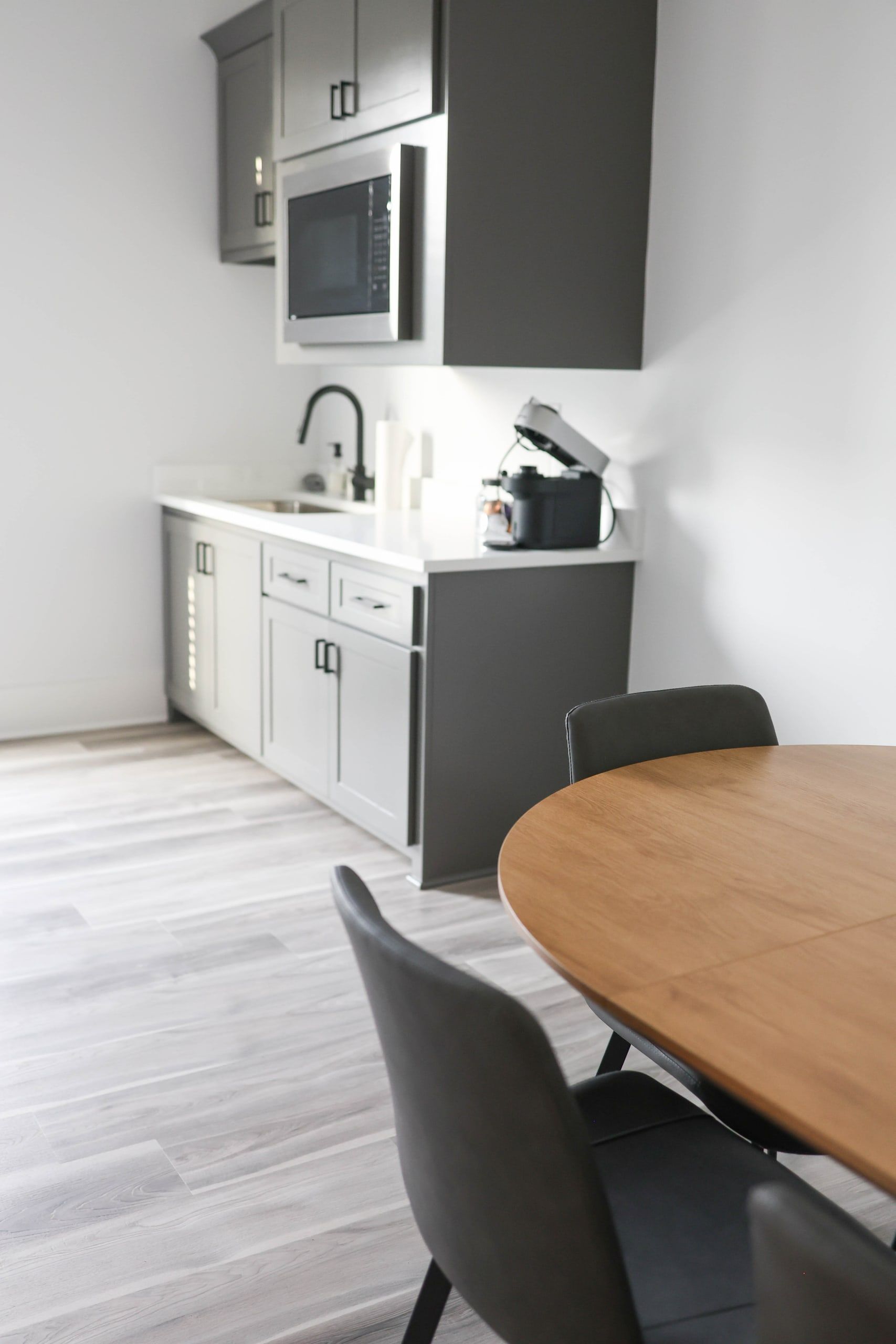 Tenant break room at The W Office Suites with a kitchenette, gray cabinets, a microwave, and a round wood table