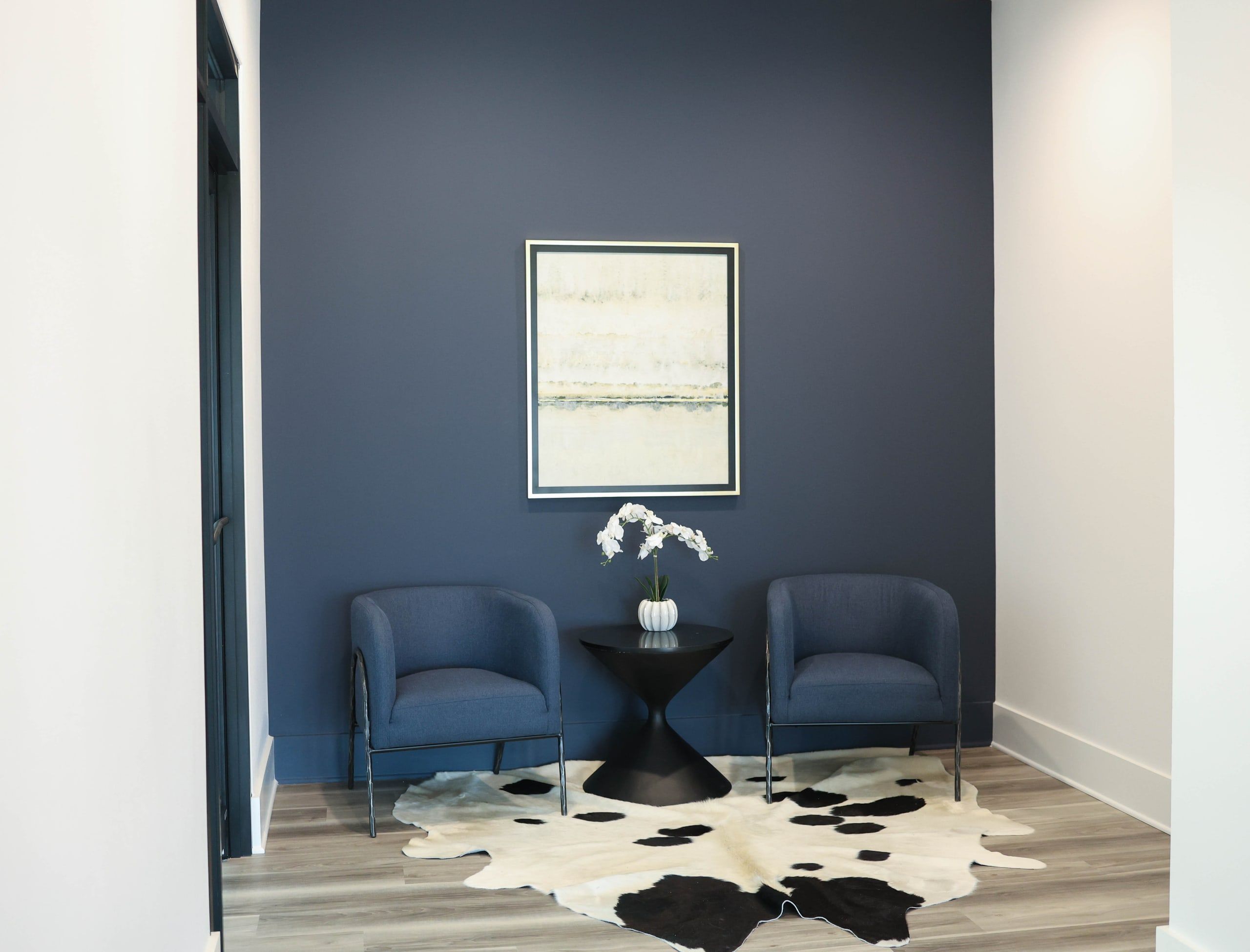 Client lounge and waiting area at The W Office Suites with two blue chairs, a cowhide rug, and framed art on a navy wall